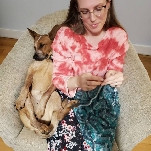 A woman knitting in a comfy chair with a sleeping dog 