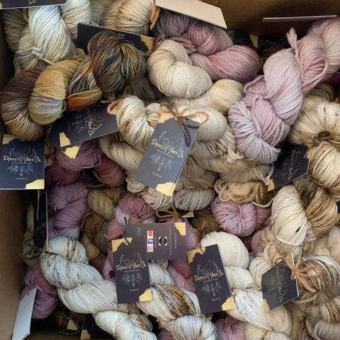 A cardboard box full of dozens of yarn skeins in browns, purples, and cream.