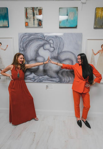 Katrina Maldova and Hannah Meorah joining outreached hands before one of Hannah's acrylic prints in Katrina's gallery.