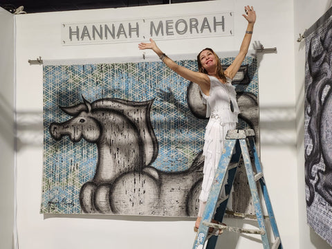 Hannah Meorah standing on a ladder installing her sensual Horse Spirit art at Art Basil.