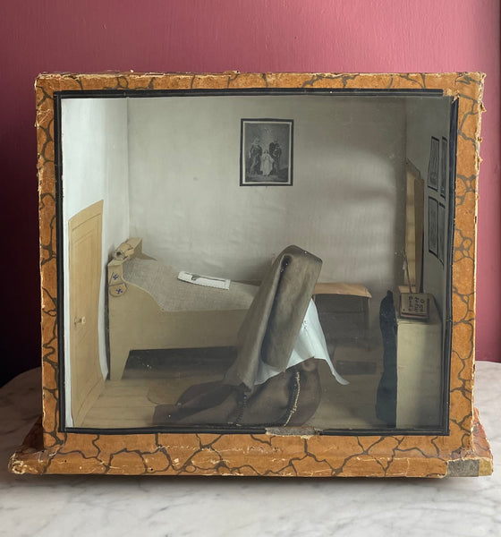 Antique diorama of a nun's cell, sparsely decorated with just a bed, chair, and altar. A praying nun figure kneels.