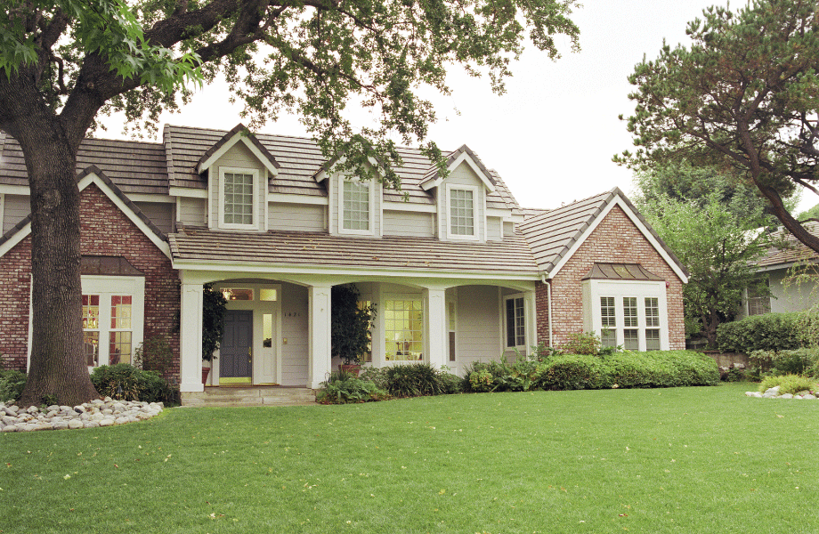 brick home with white trim with a wide green lawn and beautiful bushy garden beds with mature trees for how to add value to your home with outdoor landscaping