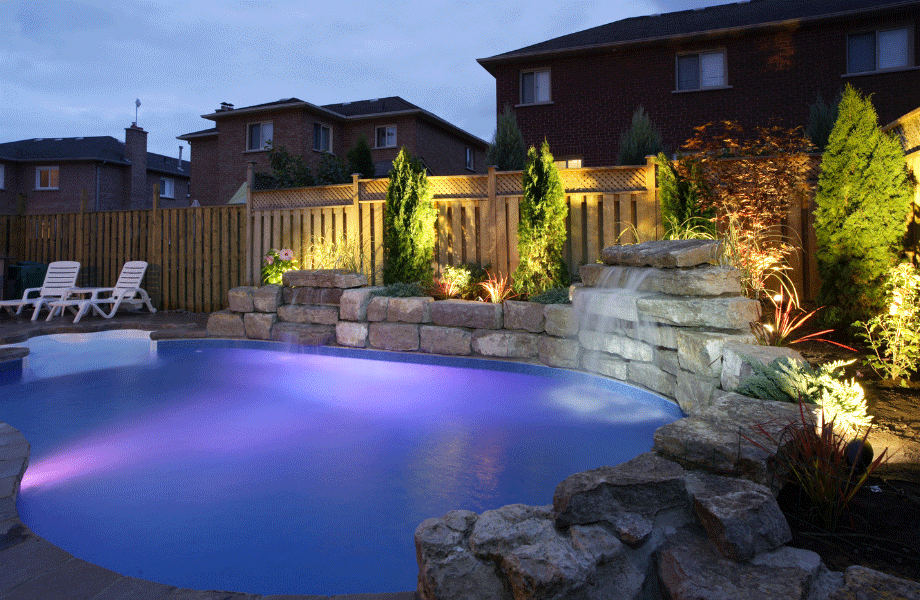 image of pool with purple lighting at dusk with rock walls and some decking and garden surrounding it for pool area ideas 