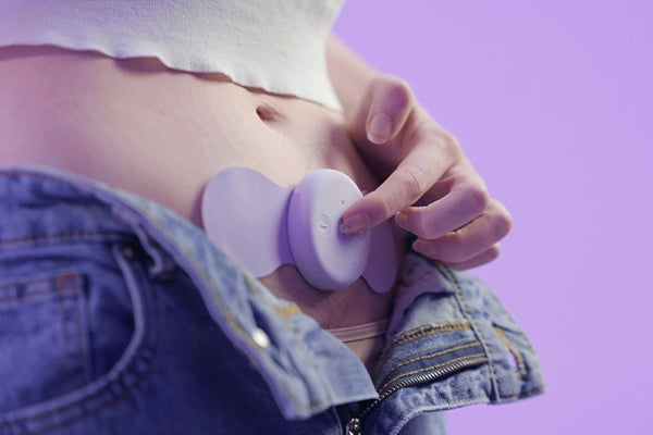 Aura pain relief device sitting on lower stomach with finger pressing on button on TENS unit