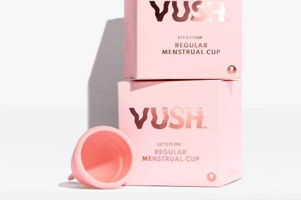 Two pink VUSH menstrual cup boxes stacked on top of one another next to pink VUSH menstrual cup