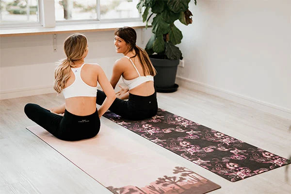 2 women sitting on yoga mats chatting before workout