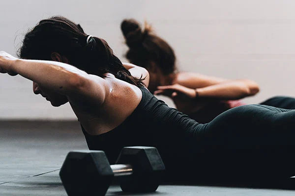 Two women lying on their stomaches with arms and chests raised working out