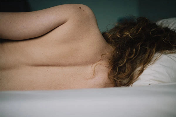 Woman lying sideways in bed topless with back facing the camera