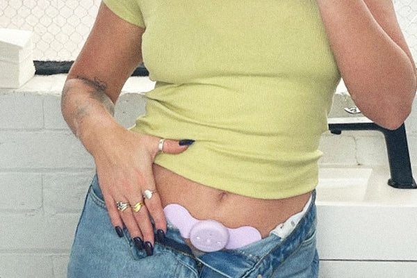 Caitlyn wearing green T shirt and blue jeans zipped open to reveal TENS machine on lower stomach