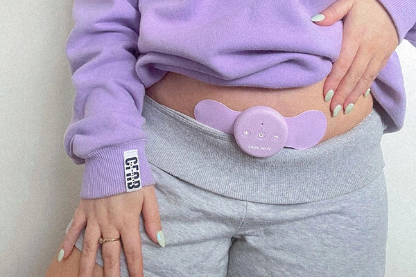 Midshot of Rachel wearing purple hoodie and grey track shorts with TENS machine on lower stomach