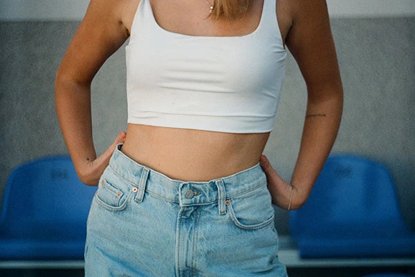 Mid-shot of woman's midriff wearing white crop top and denim shorts