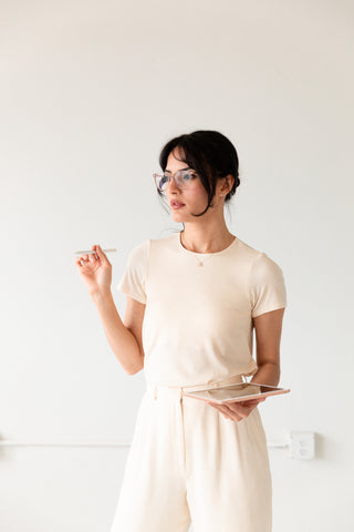 A braless woman in a workleisure blouse and glasses stands in a white office giving a presentation.