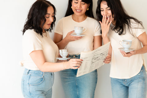 Three braless women posing in workleisure clothing in a white office..