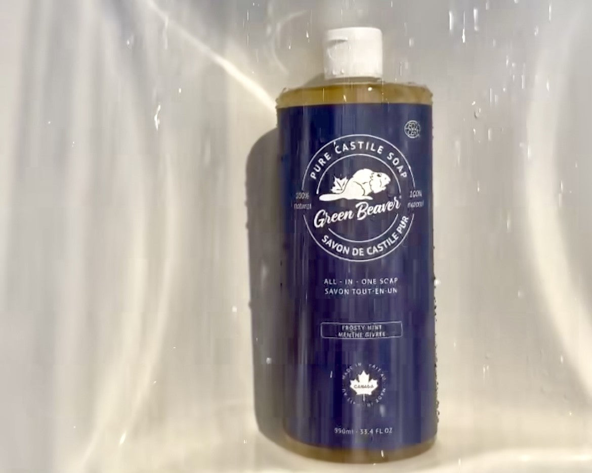 A bottle of Green Beaver's Frosty Mint Castile soap sits on a shower shelf under running water