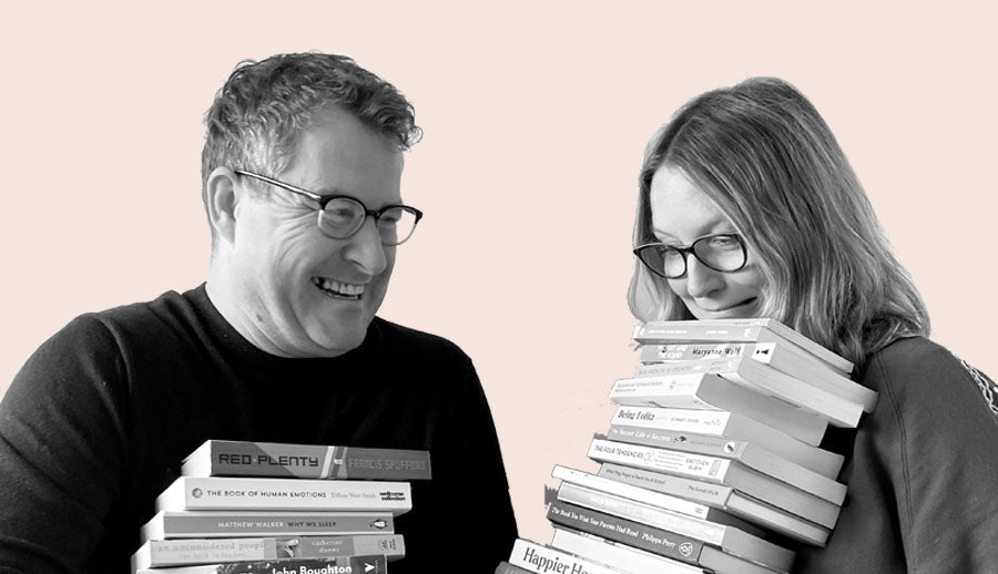 Dave and Emma are each holding a stack of non-fiction books and laughing