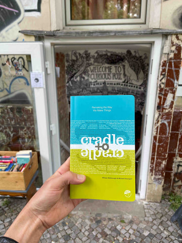 Hand holding Cradle to Cradle book in front of a Berlin bookstore.