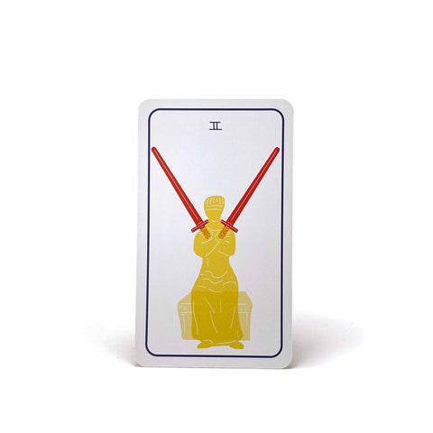 A tarot card with a roman numeral 2, showing a blindfolded woman holding swords in opposite directions. 