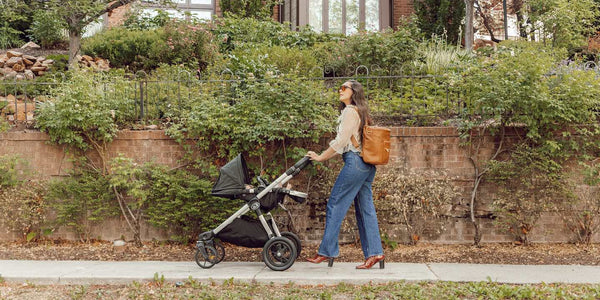 mom with a Fawn Design backpack pushing a stroller on a plant-lined sidewalk