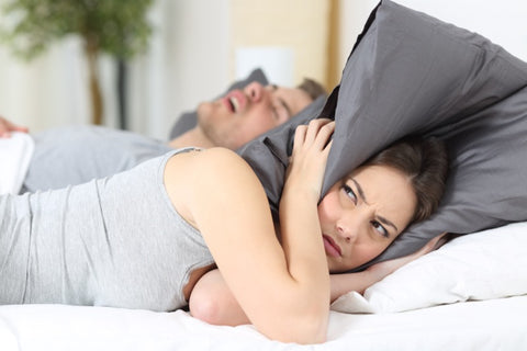 young woman covering her head with a pillow because her boyfriend is snoring loudly