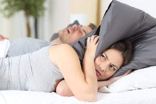 frustrated young woman with pillow over her head cannot sleep because her partner is snoring