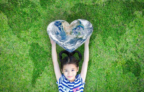 Child holding a heart shaped earth, laying on grass with map of the world