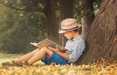 Young boy reading under a tree