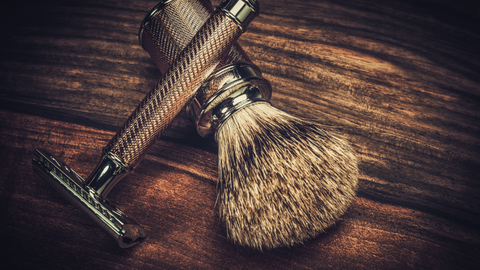 A safety razor and shave brush resting on a natural wood surface.