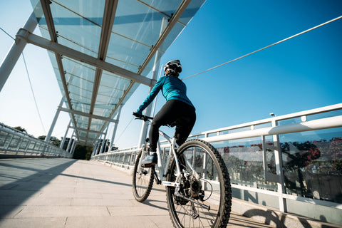 Woman riding mountain bike over urban bridge