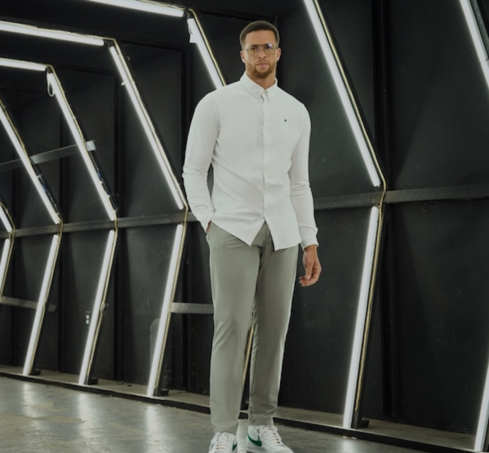 Man in white shirt and gray trousers standing in a geometric, lit hallway.