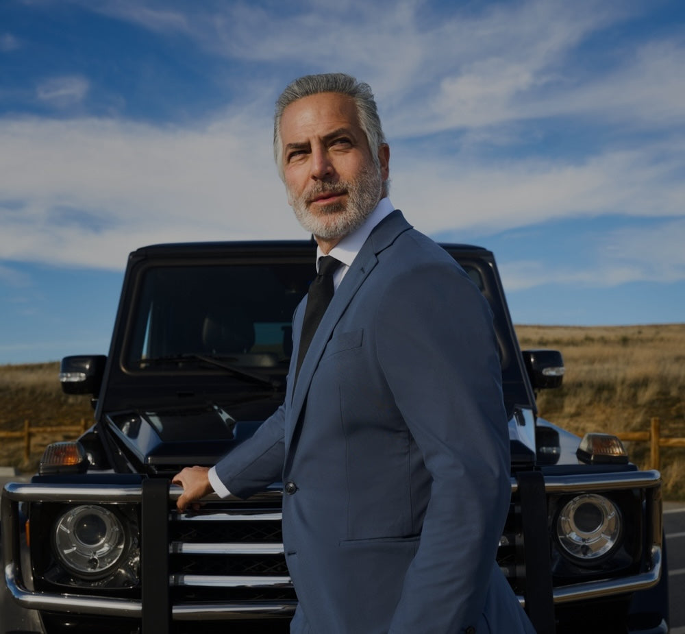 A man in a suit standing by a black luxury SUV.