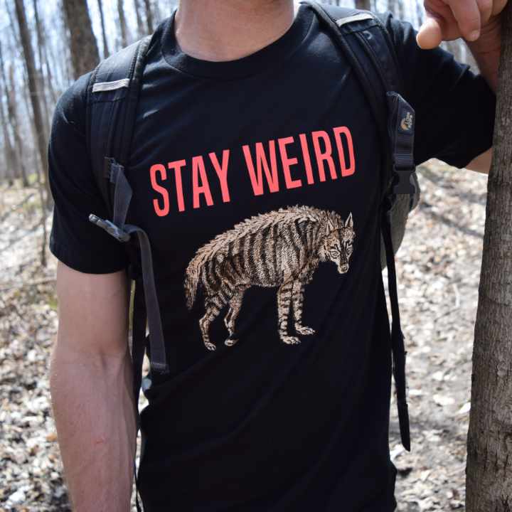 Young man wearing Rare Breed Organic Apparel's Stay Weird T-shirt in a natural forest setting