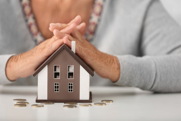 Woman's hands over a small model of a house with coins on the table.