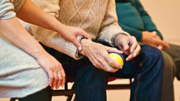 Lady holding the hand of a senior, who is holding a stress ball.