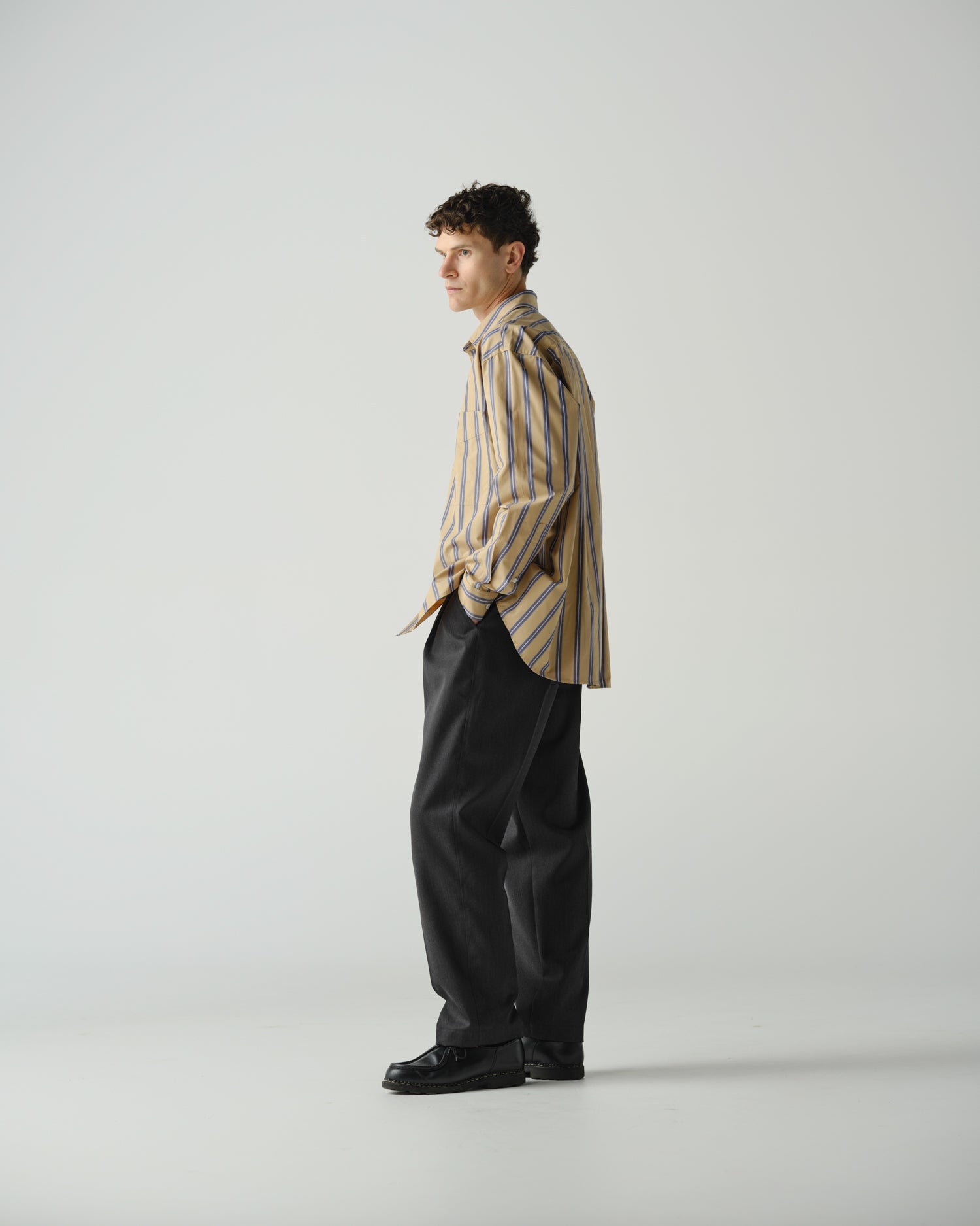 Side on view on man wearing a striped long sleeve shirt and grey tailored trouser.