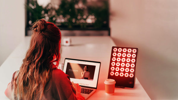 Woman using JOVS Alva Wireless LED Light Therapy Device next to laptop and coffee cup, potential Valentine's Day gift.