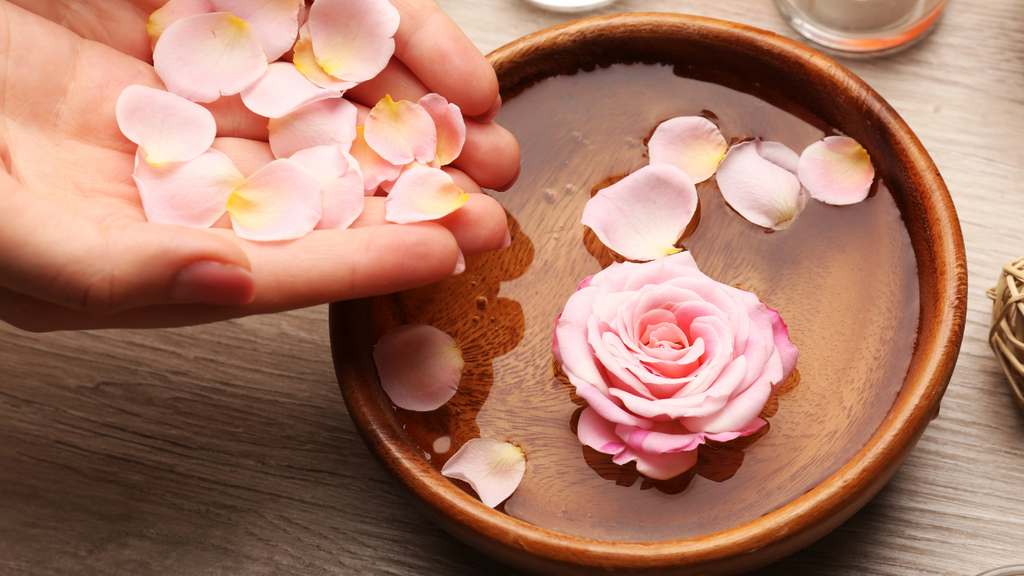 Hand scattering rose petals into water bowl with pink rose.