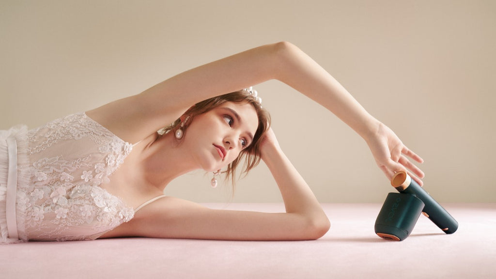 An elegant bride in a white lace dress lying on a pink backdrop, reaching out to an at home IPL hair removal device.