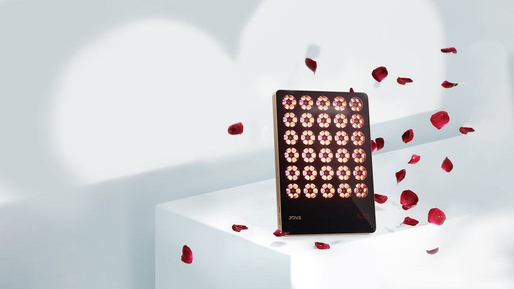 JOVS Alva Wireless LED Light Therapy Device with scattered rose petals on a white pedestal against an illuminated background.