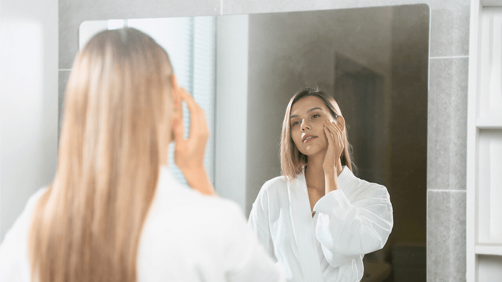 A woman examines her face in the mirror before taking a shower.