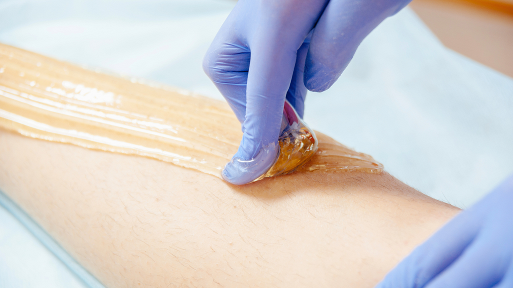 Hair removal process with sugaring paste on leg with blue gloves.