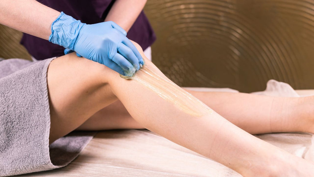 Professional applying sugaring paste for hair removal on client's leg.