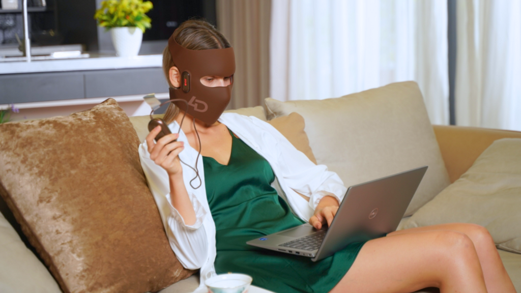 Woman wearing a light therapy mask and working on a laptop