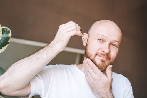 Bald man applying beard oil to his face