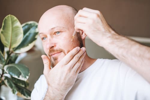 Bald man putting serum on face