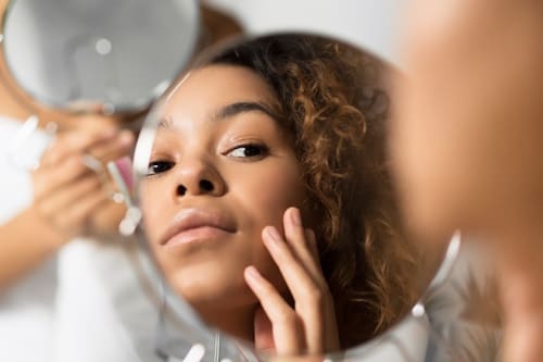 African American woman looking at her skin with table top mirror