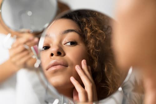 Woman looking at face skin with mirror