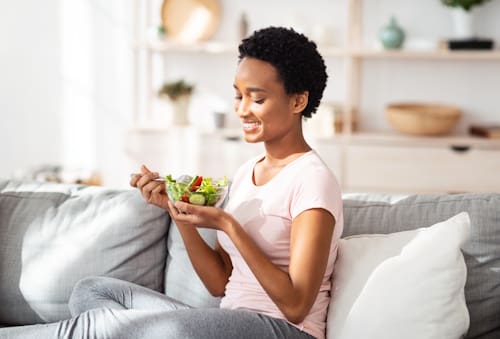 Woman on couch eating vegetables