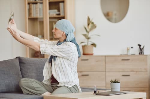 Cancer patient looking at herself with hand mirror