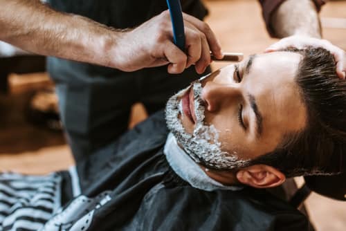 Barber shaving bearded man with shaving cream on