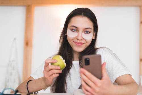 Young woman doing her skin care while eating an apple